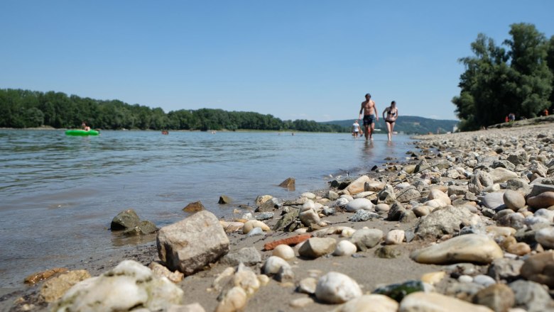 Kiesstrand am Flussufer mit Spaziergängern und einem grünen Schlauchboot., © Stadtmarketing Klosterneuburg_Leona Schwarz_td-donaustrand-klosterneuburg-c-benjamin-zibuschka